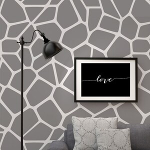 May include: A gray and white geometric pattern wallpaper with a black floor lamp and a black framed picture with the word "love" in white script. A gray couch with two gray patterned throw pillows is in the foreground.