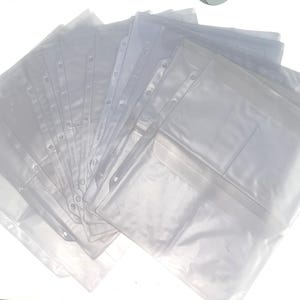 May include: A stack of clear, transparent plastic binder sleeves. Each sleeve has multiple holes along the side for insertion into a binder. Some sleeves have a pocket on the front. The sleeves are arranged in a fan shape.
