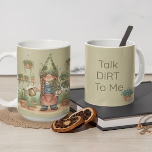 May include: Two ceramic mugs. One mug features a garden gnome with plants and a watering can. The other mug has the text "Talk DIRT To Me". The mugs are on a table with a book, dried orange slices, and glasses.