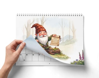 Może przedstawiać: Spiralny kalendarz 2027 Enchanted Woodland z akwarelową ilustracją gnoma z białą brodą i w czerwonej czapce w kratę. Gnom trzyma zwój z napisem 2027 ENCHANTED WOODLAND CALENDAR. Strona kalendarza zawiera widoczną siatkę z datami.