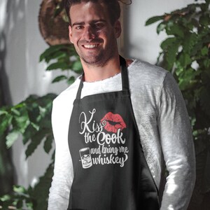 Peut inclure: Un tablier noir avec un motif blanc qui dit "Kiss the Cook and bring me whiskey". Le motif comprend également un baiser de rouge à lèvres rouge et un verre de whisky.