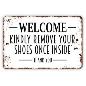 May include: A rectangular metal sign with a white background and distressed brown edges. The black text reads: WELCOME, KINDLY REMOVE YOUR SHOES ONCE INSIDE, THANK YOU. The sign features horizontal lines above and below the text for a clean look.