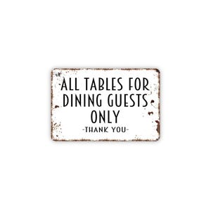 May include: A rectangular white metal sign with rounded corners and a distressed, rusted edge. The sign features black text that reads: ALL TABLES FOR DINING GUESTS ONLY -THANK YOU-. The surface has a weathered appearance with visible brown rust.