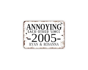 May include: A rectangular metal sign with a distressed white finish and brown rusted edges. The black text reads ANNOYING EACH OTHER SINCE 2005 RYAN & ROSANNA. The design features a vintage aesthetic with clear, bold lettering centered on the surface.