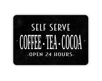 May include: A rectangular black sign with rounded corners featuring white text that reads SELF SERVE, COFFEE - TEA - COCOA, and -OPEN 24 HOURS-. The background has a subtle, fine-grained texture throughout the entire surface of the sign.