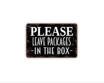 May include: A rectangular metal sign with a distressed black finish and rust-colored edges. The sign features white text that reads PLEASE LEAVE PACKAGES IN THE BOX, with small mounting holes visible on the left and right sides of the sign.