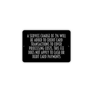 May include: A rectangular black sign with rounded corners and white text that reads: A SERVICE CHARGE OF 3% WILL BE ADDED TO CREDIT CARD TRANSACTIONS TO COVER PROCESSING COSTS. THIS FEE DOES NOT APPLY TO CASH OR DEBIT CARD PAYMENTS.