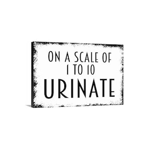 May include: A rectangular wall sign with a white background and black border featuring a distressed, weathered edge effect. The text printed in black, sans-serif capital letters reads: ON A SCALE OF 1 TO 10 URINATE, arranged in three distinct lines.