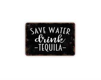 May include: A rectangular black metal sign with rounded corners and a distressed, rusted edge. The sign features white text that reads "SAVE WATER drink TEQUILA" in a combination of bold sans-serif and elegant cursive script lettering.