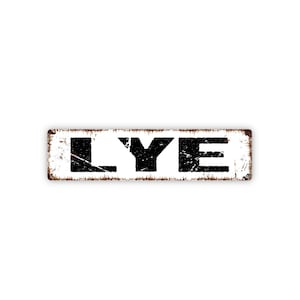 May include: Rectangular metal sign with the word "LYE" in bold, black, distressed lettering. The sign has a white background and a rusty brown border, giving it a vintage appearance.