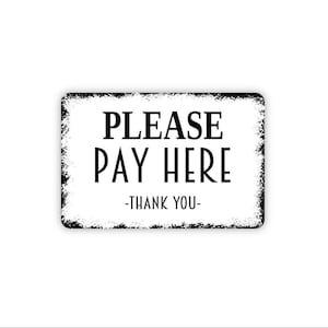 May include: A rectangular sign with a white background and black distressed edges. The text reads PLEASE PAY HERE in large black letters, with -THANK YOU- printed in smaller black letters underneath the main message on the sign.