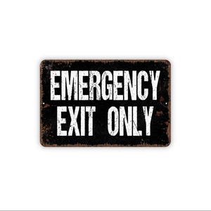 May include: A rectangular metal sign with a distressed black finish and rust-colored edges. The sign features the white, bold, sans-serif text EMERGENCY EXIT ONLY centered on the surface. The design has a weathered, vintage appearance.
