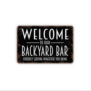 May include: A rectangular black metal sign with a distressed, rusted-look border. The white text reads: WELCOME TO OUR BACKYARD BAR PROUDLY SERVING WHATEVER YOU BRING. The sign features small mounting holes on the left and right sides for installation.