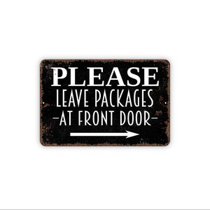 May include: A rectangular metal sign with a distressed black finish and rust-colored edges. The white text reads PLEASE LEAVE PACKAGES AT FRONT DOOR, accompanied by a white horizontal arrow pointing to the right, indicating delivery instructions.