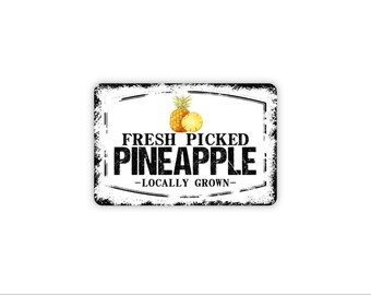 May include: A rectangular metal sign with a white background and black distressed edges. It features a yellow pineapple illustration and black text that reads FRESH PICKED PINEAPPLE -LOCALLY GROWN- in a mix of serif and bold sans-serif fonts.