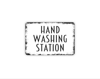 May include: A rectangular sign with a white background and black border featuring distressed edges. The text HAND WASHING STATION is printed in the center in a bold, black, sans-serif font. The sign has rounded corners and a clean, high-contrast design.