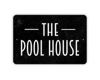 May include: A rectangular black sign with rounded corners featuring the white text THE POOL HOUSE in a clean sans-serif font. The background has a subtle, fine-grained texture, and there are two small mounting holes on the left and right sides.