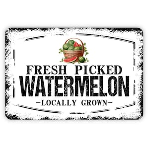 May include: A rectangular metal sign with a distressed white background and black border. The center features a basket of green watermelons and a slice of watermelon. The text reads FRESH PICKED WATERMELON LOCALLY GROWN in black lettering.