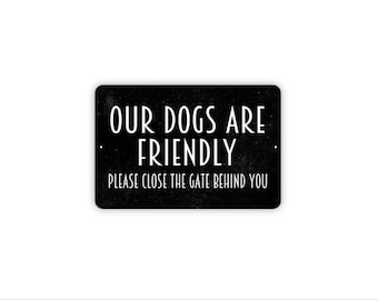 May include: A rectangular black sign with white text that reads OUR DOGS ARE FRIENDLY and PLEASE CLOSE THE GATE BEHIND YOU. The sign features a textured finish and two small mounting holes on the left and right sides for installation.