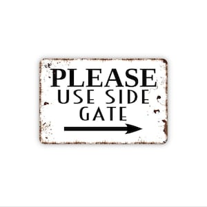 May include: A rectangular metal sign with a white background and distressed brown edges. The sign features black text that reads PLEASE USE SIDE GATE, accompanied by a black arrow pointing to the right, indicating the direction to the side gate.