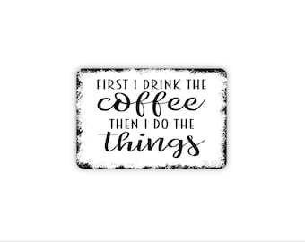 May include: A rectangular white metal sign with distressed black edges featuring the black text FIRST I DRINK THE coffee THEN I DO THE things. The word coffee is in a cursive script font, while the other words are in a sans-serif font.