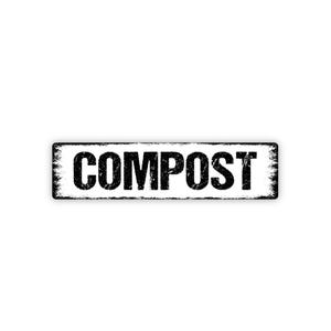 May include: A rectangular black and white sign with the word "COMPOST" in bold, distressed font. The sign has a weathered, vintage look, with a white background and a black border.