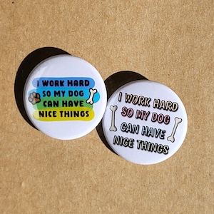 May include: Two white round buttons with the text "I work hard so my dog can have nice things" in rainbow colors. The text is surrounded by a paw print and bone graphic.