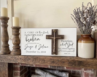 May include: A wooden sign with a cross and text, "A cord of three strands is not easily broken." The sign includes the names Jorge & Jolene and the date December 11, 2010. Two wooden candle holders with candles are on the left.