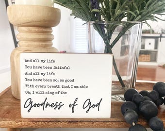 May include: A rectangular white wooden sign with black text that reads: And all my life, You have been faithful, And all my life, You have been so, so good, With every breath that I am able, Oh, I will sing of the Goodness of God.