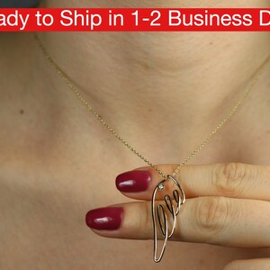 Può includere: Una collana d'oro con un delicato ciondolo a forma di ala con una piccola pietra trasparente. Il ciondolo è tenuto da una mano con smalto rosso.