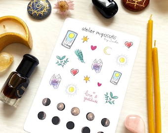 May include: An assortment of spiritual items including a sticker sheet with illustrations, crystals, candles, a bottle of perfume, a piece of palo santo, and decorative stones. The sticker sheet features the text "atelier myosotis" and "love & gratitude".