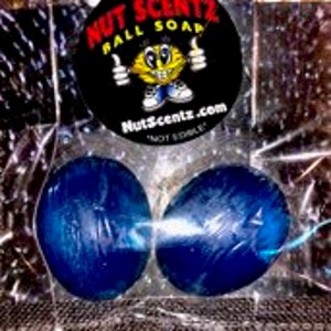 Puede incluir: Dos barras de jabón ovaladas azules en una bolsa de plástico transparente con una pegatina redonda que dice "NUTZ SCENTZ BALL SOAP" con un personaje de dibujos animados y el sitio web "nutzscentz.com".
