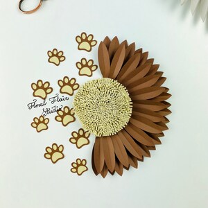 May include: A brown paper flower with a yellow center, surrounded by small yellow paw print cutouts. The text "Floral Flair Studio" is written in cursive on the white background.