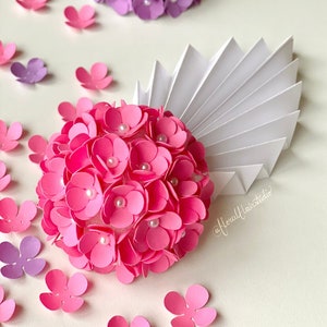 Peut inclure: Deux arrangements de fleurs en papier, l'un rose et l'autre violet, avec des accents de perles blanches. Les fleurs sont dispos&eacute;es en forme de sph&egrave;re et sont entour&eacute;es de plus petites fleurs en papier.