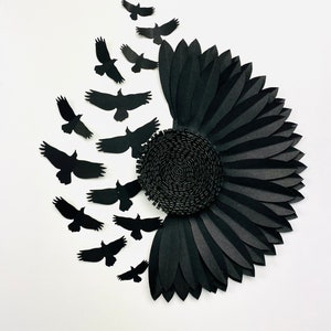 May include: A black paper sunflower with a spiral center and layered petals. Silhouettes of black birds are arranged to the left, appearing to fly away from the flower. The artwork is set against a white background.