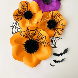 K&ouml;nnte beinhalten: Drei gro&szlig;e Papierblumen mit schwarzen Spinnweben darauf. Die Blumen sind orange und lila. Es gibt auch mehrere schwarze Papierflederm&auml;use auf wei&szlig;em Hintergrund.