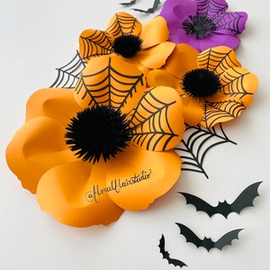 K&ouml;nnte beinhalten: Orangefarbene und violette Papierblumen mit schwarzen Spinnweben und Flederm&auml;usen. Die Blumen sind &uuml;bereinander gelegt und haben einen 3D-Effekt. Die Flederm&auml;use sind aus schwarzem Papier ausgeschnitten und fliegen in der Luft. Die Blumen sind mit schwarzen Pompons in der Mitte verziert.