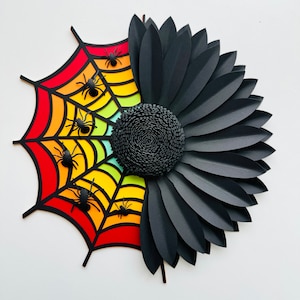 May include: A colorful rainbow spiderweb with black spiders and a black paper flower with a black center.