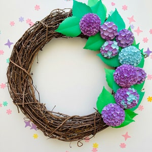 Peut inclure: Une couronne de branches brunes d&eacute;cor&eacute;e d'hortensias en papier dans des tons de violet et de bleu. La couronne est entour&eacute;e de fleurs en papier &eacute;parpill&eacute;es dans diff&eacute;rentes couleurs.