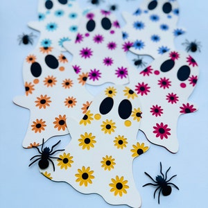 May include: Five white ghost cutouts with different floral patterns. The ghosts are arranged in a semi-circle with black spiders scattered around them.