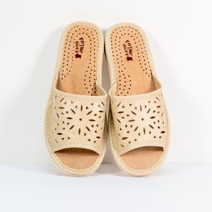 May include: A pair of beige leather slippers with a floral cut-out design. The slippers have a brown leather insole with the text "Fajne Buty" printed on them.