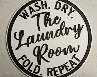 May include: A round white sign with a black border and black text that reads "Wash. Dry. The Laundry Room. Fold. Repeat."
