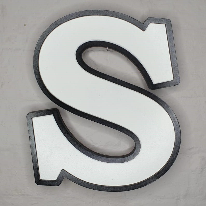 May include: A large, white letter S with a black outline. The letter is made of wood and has a vintage look.