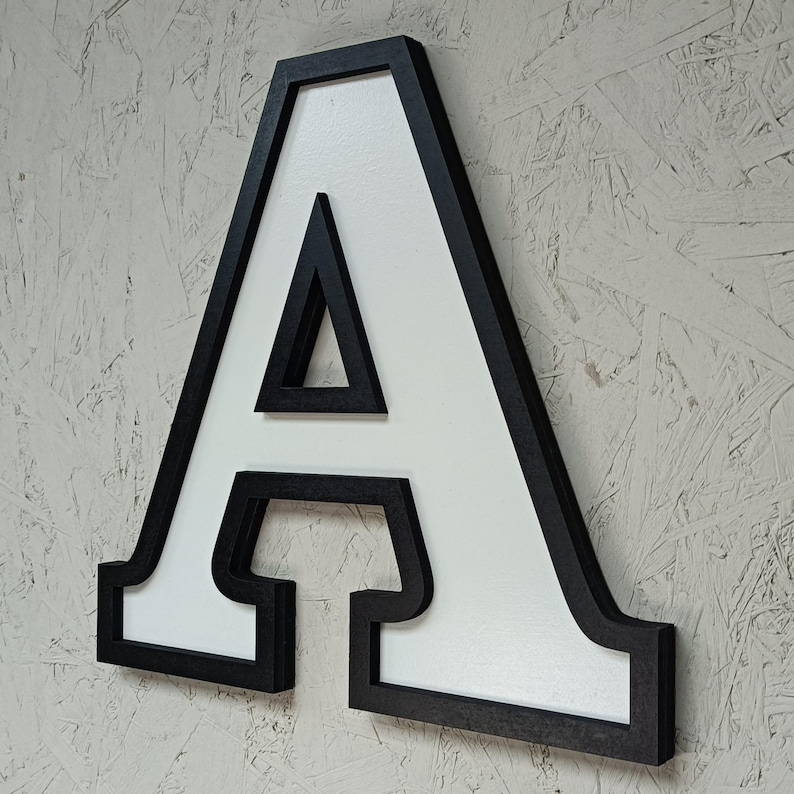 May include: A large, white wooden letter A with a black outline. The letter is three-dimensional and has a shadow behind it.