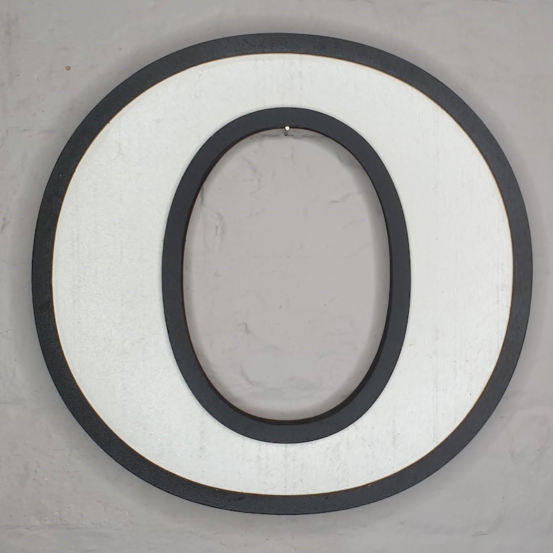 May include: White wooden letter O with a black outline. The letter is painted white and has a black border around the outside edge and around the inside of the letter.