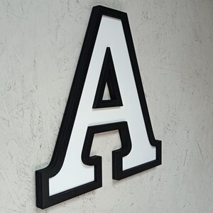 May include: A large, white, wooden letter A with a black border. The letter is three-dimensional and has a shadow behind it.