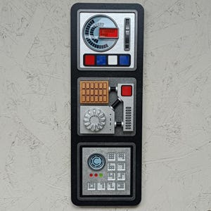 May include: A black control panel with a silver dial, buttons, and a series of switches. The panel has a red, white, and blue colour scheme.