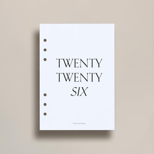 May include: A white planner insert featuring the text "TWENTY TWENTY SIX" in black. The insert has six pre-punched holes for binding. The text "The Peacocke Collector" is printed at the bottom of the page.