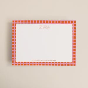 May include: A rectangular notepad with a pink and orange checkered border. The notepad has a white interior with the text "FROM THE DESK OF LILA PINNOCK" and an address printed in a small font.