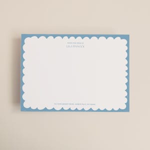 Op de afbeelding: Een rechthoekige briefkaart met een geschulpte lichtblauwe rand. De kaart bevat de tekst "FROM THE DESK OF LILA PINNOCK" en een adres onderaan. De achtergrond is wit.